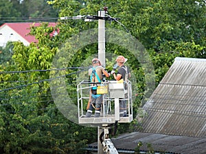 Two electricians repair high voltage power lines. Technology of work on electric poles in the city. Safety precautions for work at