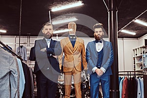 Two elegantly dressed shop assistants posing near mannequin in menswear store.