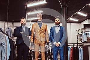 Two elegantly dressed shop assistants posing near mannequin in menswear store.