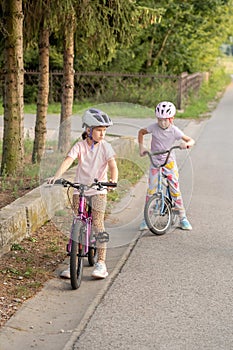 Two elementary school age girls, children biking, cycling, riding their bikes on a country road in a rural area together Friends,