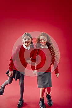 Two Elementary School Pupils Wearing Uniform Linking Arms Against Red Studio Background