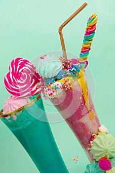 Two elicious homemade extreme milkshake, with a blackberry candy over a milk foam and a rainbow candy on top with a