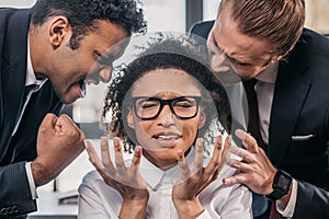 Two emotional businessmen in formalwear screaming on businesswoman in office