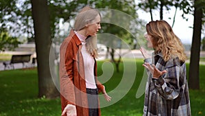 Two emotional Caucasian women arguing outdoors talking gesturing in slow motion. Side view portrait of unsatisfied young