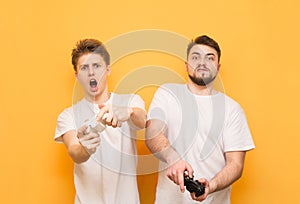 Two emotional men, a teenager and a man with a beard, are on a yellow background with joysticks in their hands and expressively
