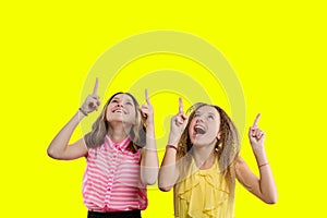 Two emotional teenage girls showing and looking up, copy space yellow background