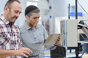 two employees using tablet and computer keyboard in workshop