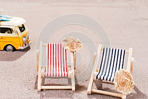 Two empty beach chairs in the sand, with old van