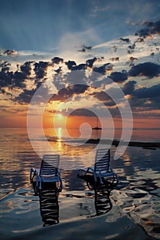 Two empty beach chairs with shade in the water the beach at suns