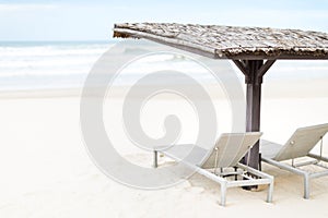 Two empty chaise longues under shed on beach.