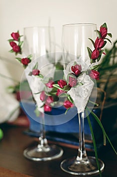 Two empty champagne glasses decorated with white lace and red roses flowers on hotel room table, morning wedding preparation