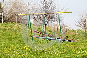 Two empty children swings and seesaw at playground activities in public park / Natural environment, grass, spring flowers.