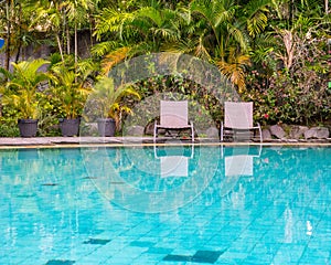 Two empty deck chairs next to the garden and pool in late afternoon