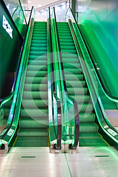 Two empty escalator stairs are illuminated with green light. Descent and ascent