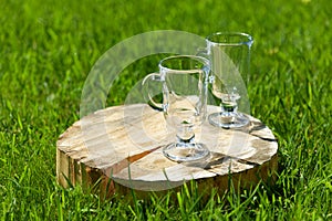 Two empty glass glasses with a handle stand on a cracked wooden stand on a green lawn on a Sunny summer day