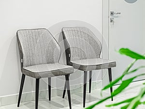 Two empty gray designer chairs, closed door with key and green houseplant in the foreground in a medical waiting room in a white c