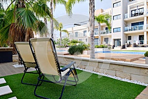 Two empty lounge chairs on artificial lawn grass inside of personal area backyard residential summer villa