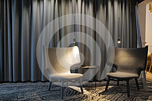 Two empty modern grey chair with lights and a table between. Curtains on a background