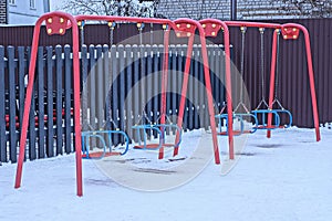 Two empty red metal swings on a playground in white snow