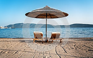 Two empty sun beds deck chairs under umbrellas on an empty sandy beach with sea views