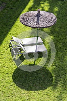 Two empty sunbeds on a green field with an umbrella, ready for people to relax and take a sunbath