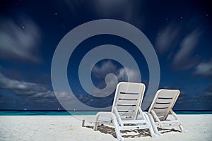 Two empty sunbeds on the ocean beach under night sky with stars