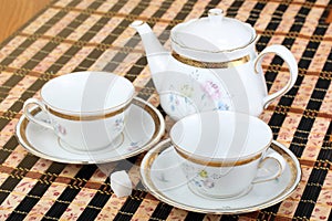 Two empty white porcelain cup and teapot on the table covered with striped table mat