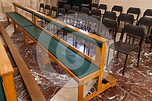 Two empty wooden pews in a church with chairs