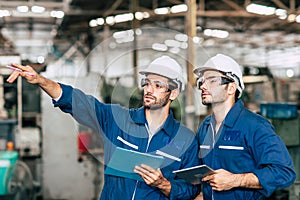 Two engineer worker working together with safety uniform and white helmet to work in industry checking production line