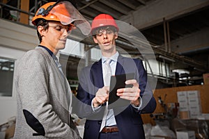 Two engineers discuss a project using a tablet while they are in the factory