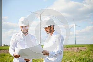 Two engineers discussing against turbines on wind turbine farm.