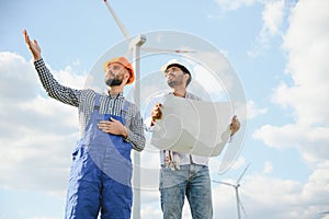 Two engineers discussing against turbines on wind turbine farm.