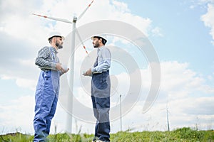 Two engineers discussing against turbines on wind turbine farm.