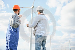 Two engineers discussing against turbines on wind turbine farm.