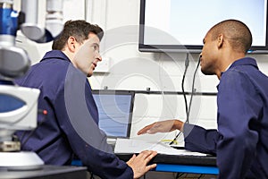 Two Engineers Discussing Plans With CMM Arm In Foreground