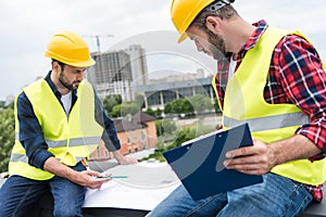 two engineers in helmets working with blueprints and clipboard