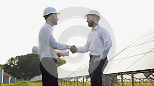 Two engineers, investors or businessmen shaking hands after discussion on background of photovoltaic solar panels