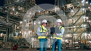 Two engineers with a laptop are talking inside of the oil refinery