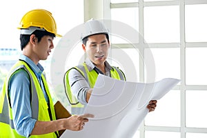 Two engineers man standing in front of the site. Left engineer holding blueprint diagram