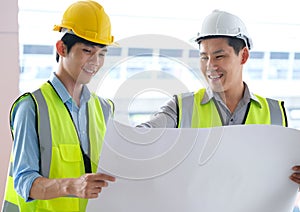 Two engineers man standing in front of the site. Left engineer holding blueprint diagram