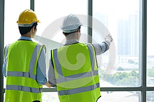 Two engineers man standing in front of windows. Left engineer holding blueprint diagram