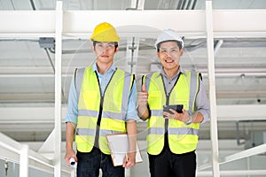 Two engineers man standing in the site. Engineer holding  tablet and smile and thumbs up and other engineer holding chart