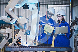 Two engineers mechanic using computer controller Robotic arm for welding steel in steel factory workshop. Industry robot