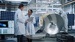 Two Engineers Talk, Use Tablet Computer while Working on Satellite Construction. Aerospace Agency