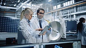 Two Engineers Talk, Use Tablet Computer while Working on Satellite Construction. Aerospace Agency
