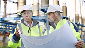 Two engineers are talking in front of electrical transmission lines, working on renewable energy development. Engineers