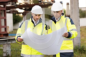 Two engineers are talking in front of electrical transmission lines, working on renewable energy development. Engineers