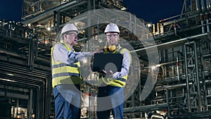 Two engineers are talking inside of the oil refinery plant. Oil industry, petrochemical factory, refinery concept.