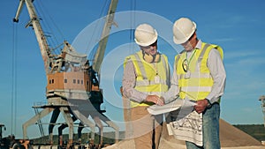 Two engineers are talking next to loading cranes