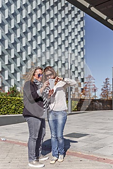 Two enterprising women with casual clothes, look at something on a mobile device in a street